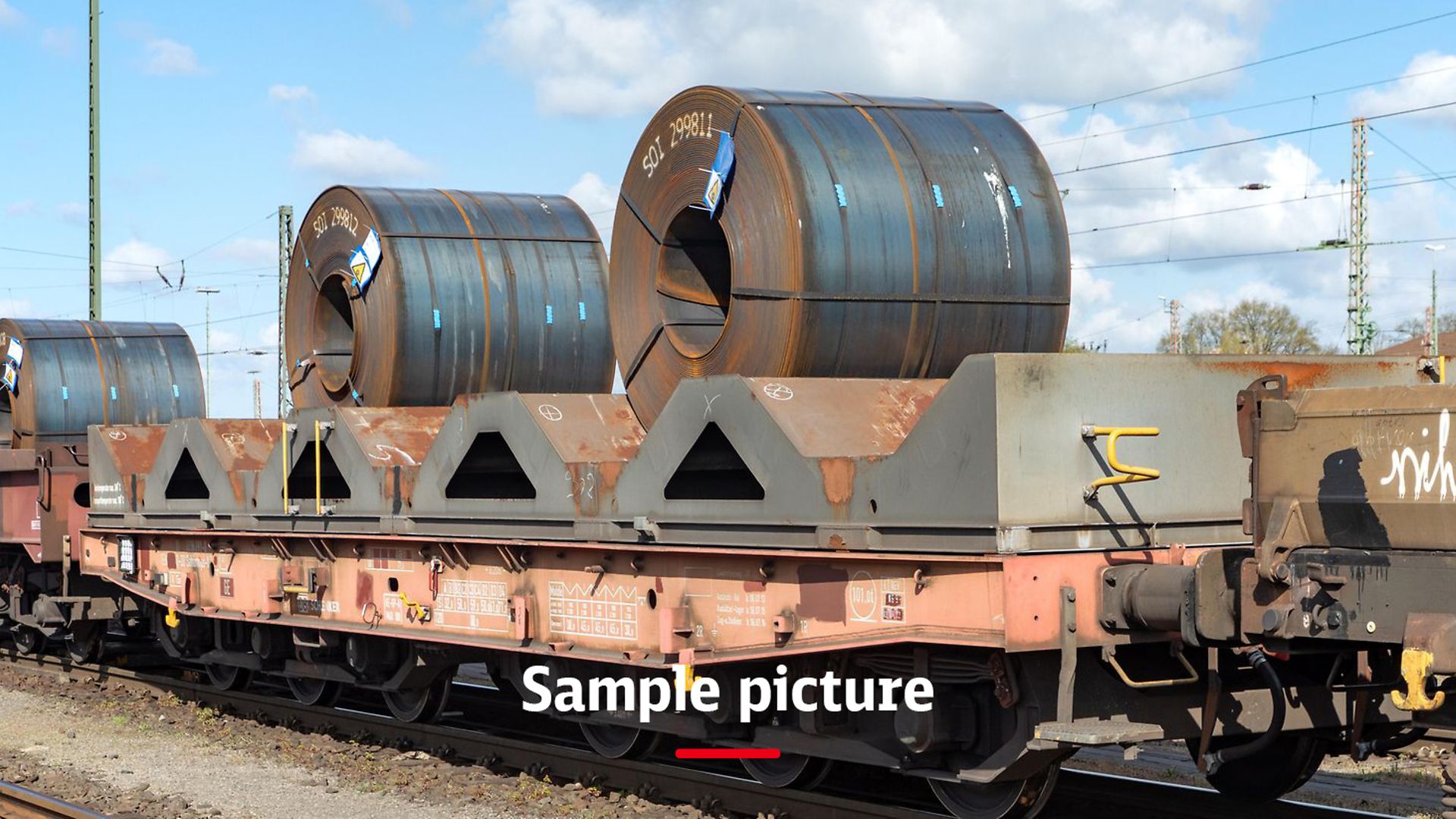 A freight train with wagons loaded with steel rolls and the signature Sample picture